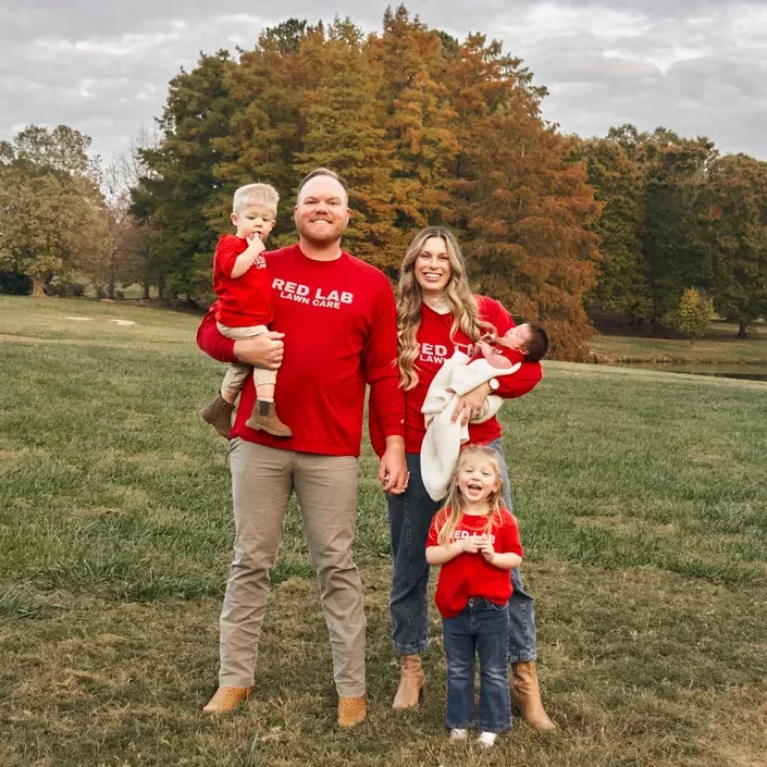 A family is standing in a field wearing red sweaters.